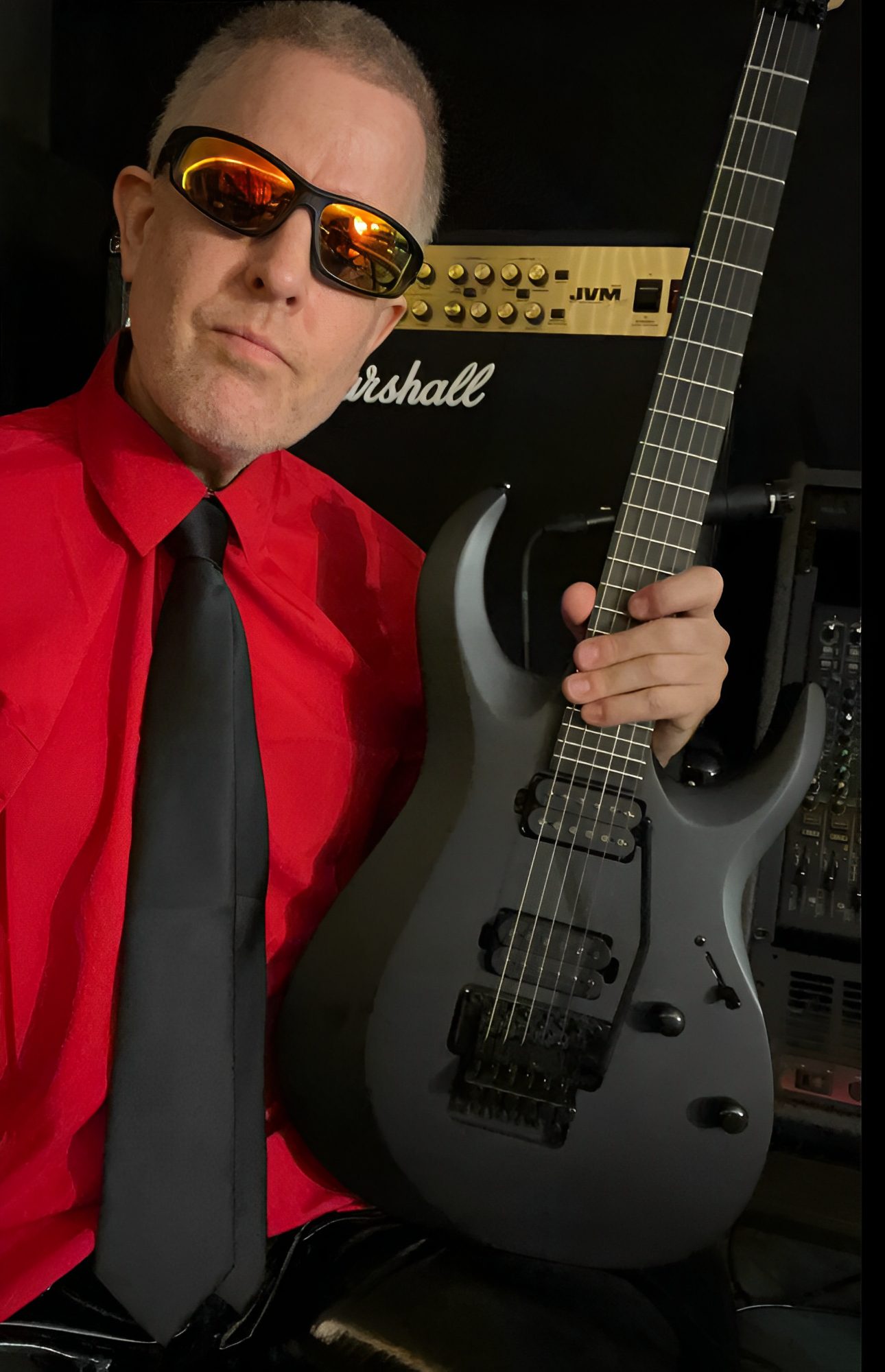 Man in sunglasses holding a black guitar.